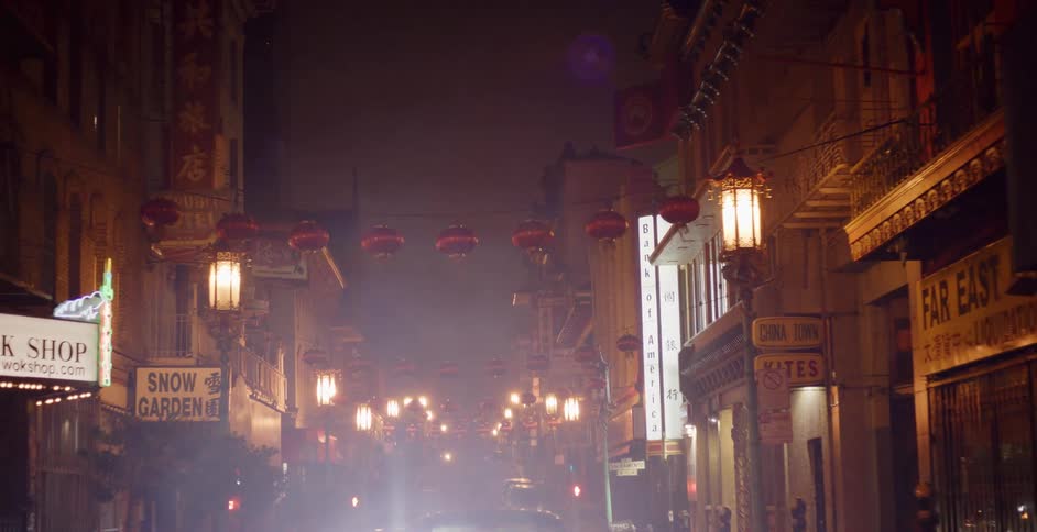 A slow, cinematic pull-back reveals a classic car parked on a foggy Chinatown street at night, illuminated by its bright headlights and red lanterns