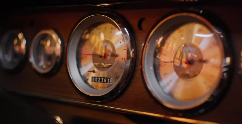Warm light reflects off the classic chrome gauges and wooden dashboard of a vintage car