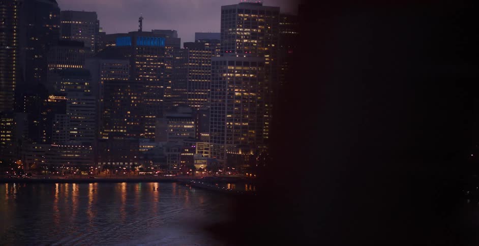 A dramatic panning shot reveals the glowing San Francisco skyline and waterfront at twilight from across the bay