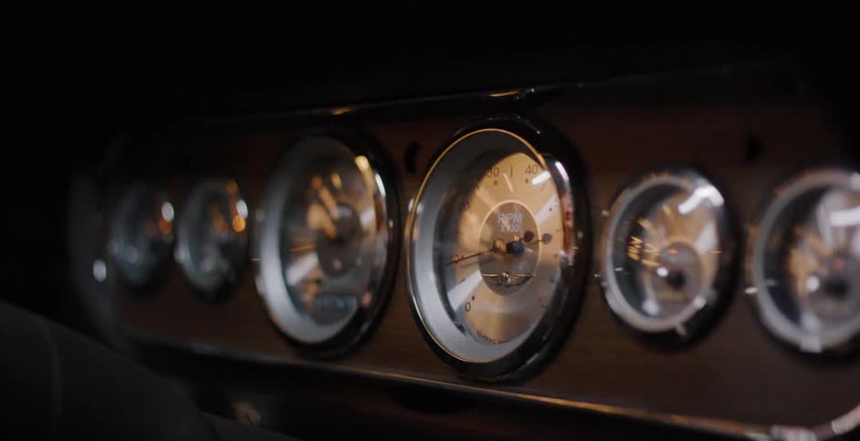A slow pan across the stylish, chrome-rimmed analog gauges on the dashboard of a classic car