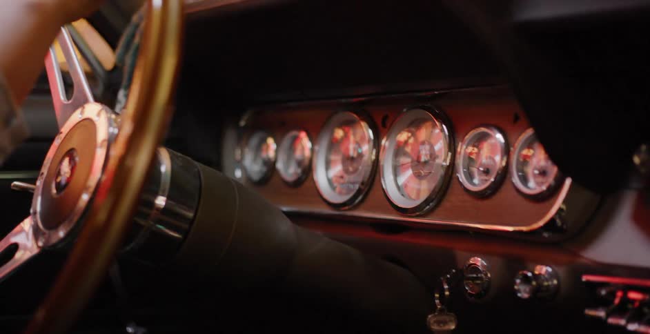 The stylish wood and chrome dashboard of a vintage muscle car reflects passing lights at night