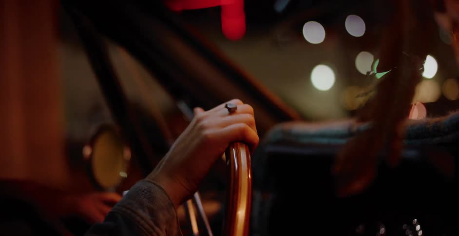 A moody close-up of a driver's hand on the steering wheel of a vintage car during a nighttime city drive