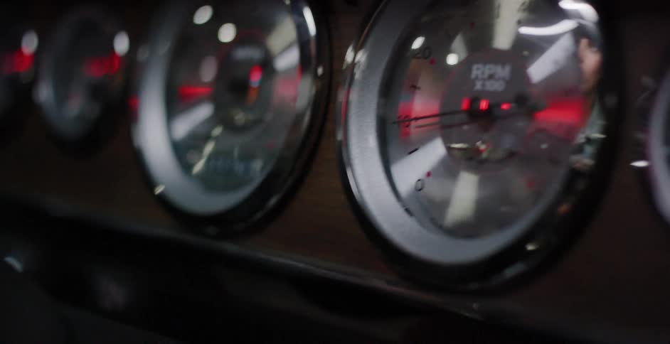 The vintage dashboard gauges of a classic car reflect lights as the vehicle is in motion