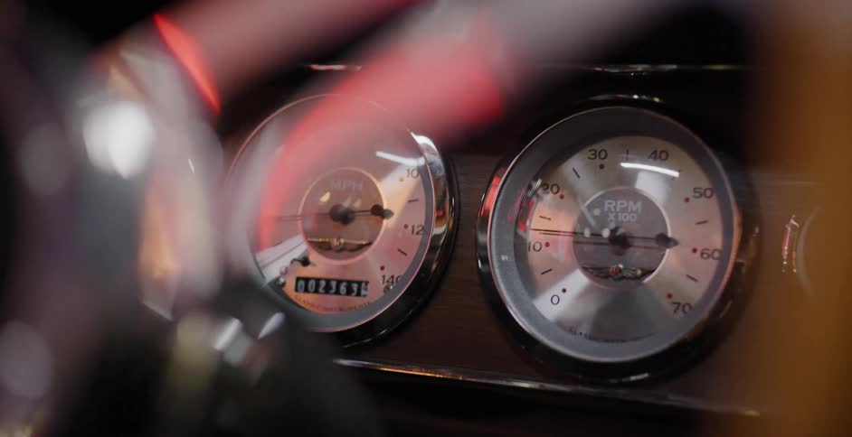Artistic close-up shot of a vintage car's instrument panel, featuring the classic speedometer and tachometer seen through reflective light flares