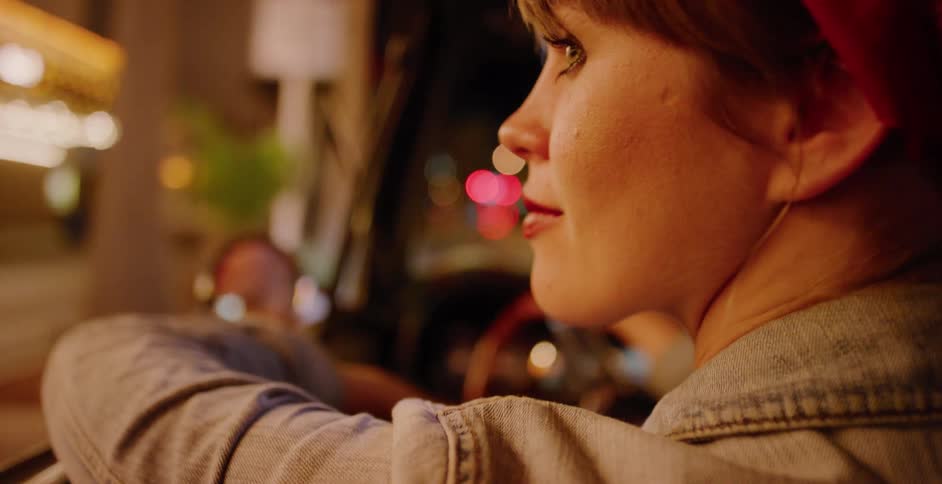 A stylish woman drives through the city at night, with a close-up shot on her face as the colorful streetlights create a beautiful bokeh effect