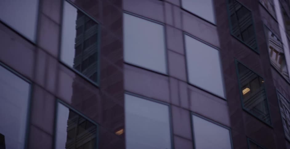 Moody shot panning from a modern glass skyscraper reflecting the city to an adjacent concrete office building at dusk