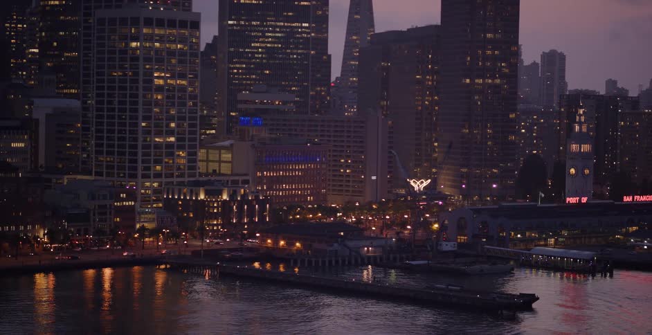 Slowly panning across the illuminated San Francisco cityscape and Embarcadero waterfront at dusk