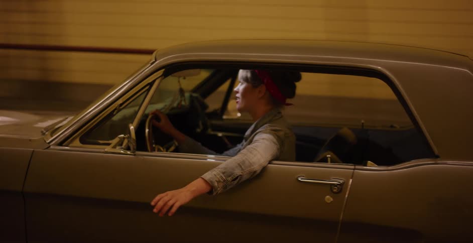 A stylish woman enjoys a carefree night drive in her classic Ford Mustang through an illuminated tunnel, her arm hanging out the window