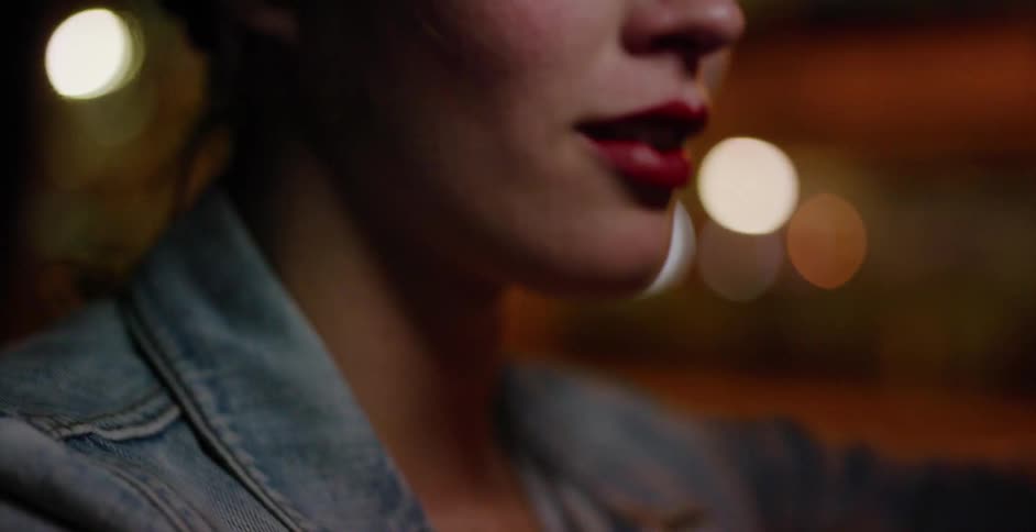 A cinematic close-up of a woman's mouth with red lipstick as she sits in a car driving through the city at night