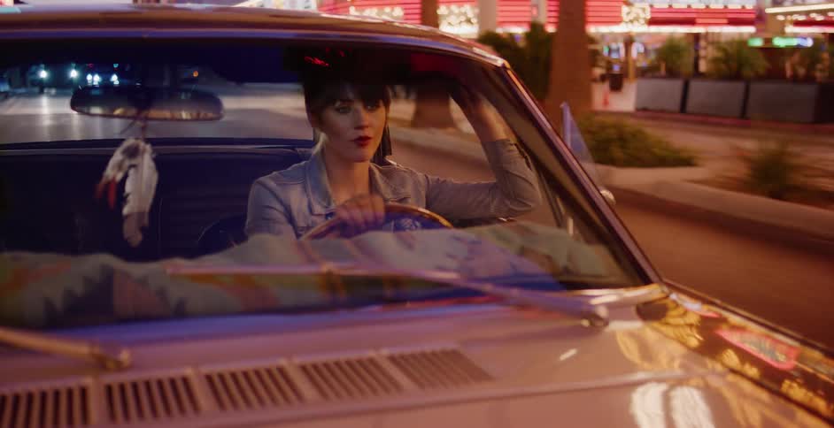 A stylish woman drives a vintage car down a neon-lit city street at night, looking out the window
