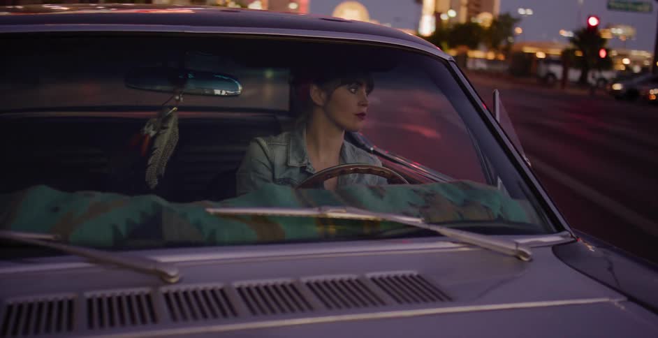 A young woman drives her classic purple muscle car through the city at night