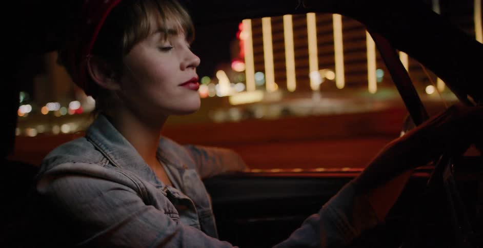 A stylish woman in a retro outfit drives her classic car through the glowing city lights at night