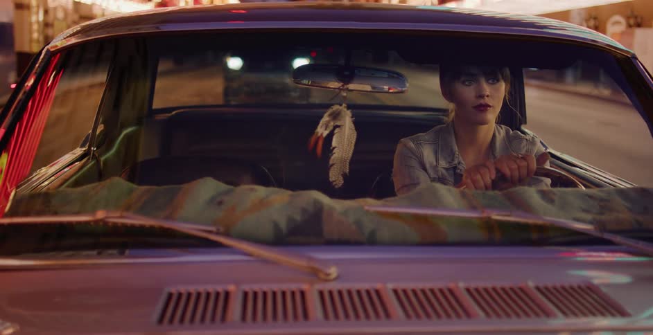A young woman drives a classic car through the neon-lit streets of Las Vegas at night