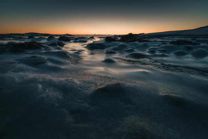 A slow pull-back shot reveals a vast, frozen landscape covered in snow and ice during a serene winter sunset