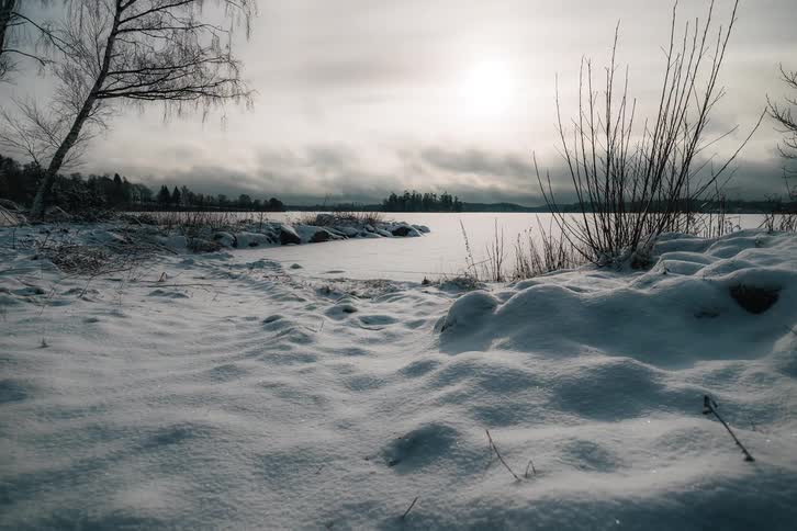A serene timelapse captures clouds moving across the sky over a frozen lake on a cold, snowy winter day