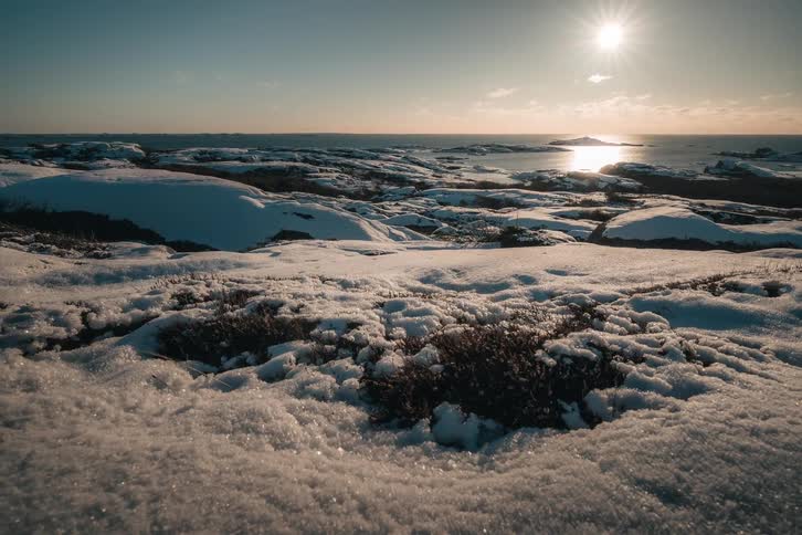Time-lapse of the winter sun moving across a snow-covered rocky coastline, with its light reflecting on the calm ocean