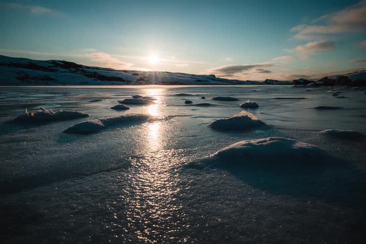 A serene timelapse captures the setting sun's reflection on a vast, frozen, and snow-dusted landscape