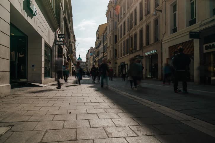 A dynamic low-angle time-lapse captures the fast-paced flow of people on a historic European city shopping street