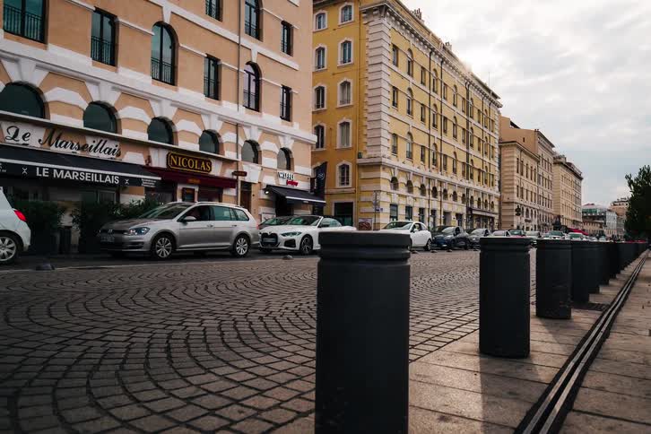 A slow zoom-out time-lapse captures the blur of traffic on a historic cobblestone street in Marseille, France
