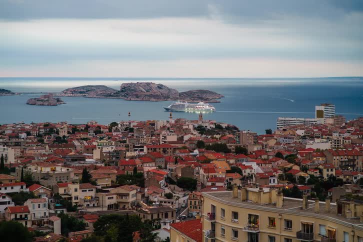 A twilight timelapse of a large cruise ship sailing away from the coastal city of Marseille, France, with islands in the background