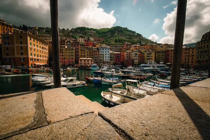 A scenic timelapse from a stone pier captures the vibrant harbor of Camogli, Italy, as boats sway in the turquoise water and clouds move across the sky