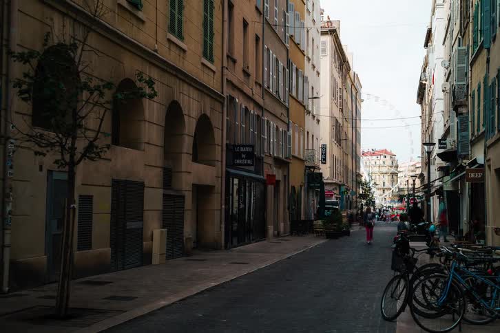 A long exposure timelapse shows the bustling activity on a classic European street in Marseille, France, as people and shadows move throughout the day
