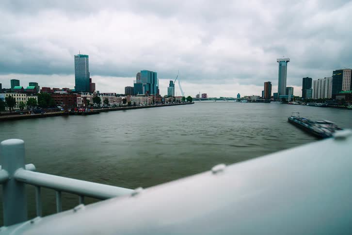 A dramatic timelapse reveals the bustling Nieuwe Maas river in Rotterdam, with boats speeding past the modern skyline under a cloudy sky