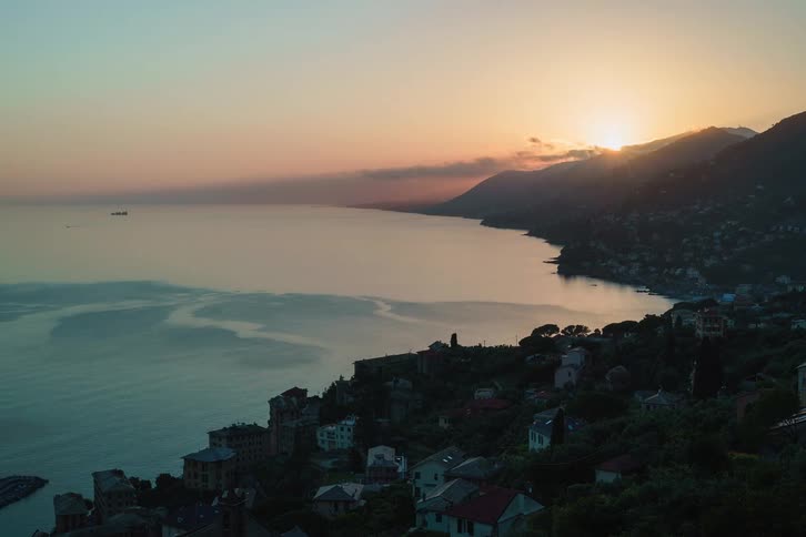 A stunning time-lapse captures the sun setting behind the mountains over a picturesque Italian coastal town and the sea