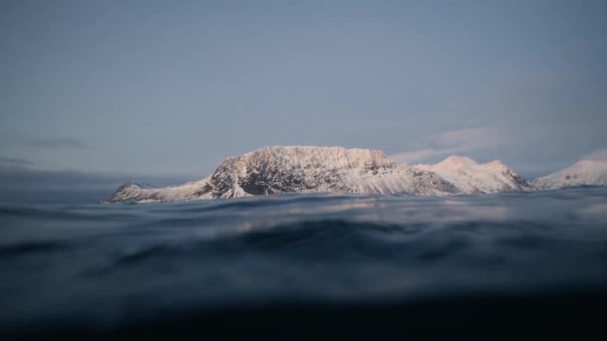 A serene split-level perspective from the surface of the ocean reveals a majestic snow-covered mountain range