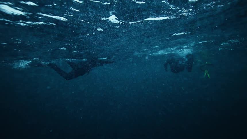 Slow motion underwater view of several free-divers swimming on the surface of the deep blue ocean