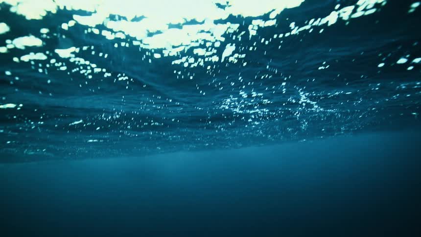 An underwater perspective of the deep blue ocean surface as it gently ripples in slow motion