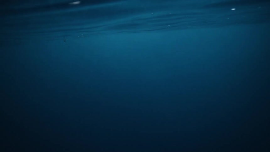 A serene underwater view looking up at the surface of the deep blue ocean as it gently ripples