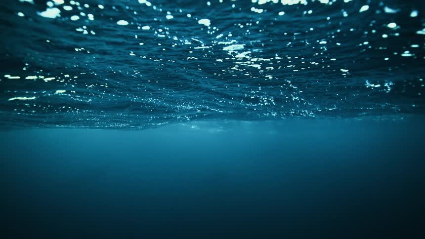 A serene underwater perspective captures sunlight glistening on the rippling surface of the deep blue ocean