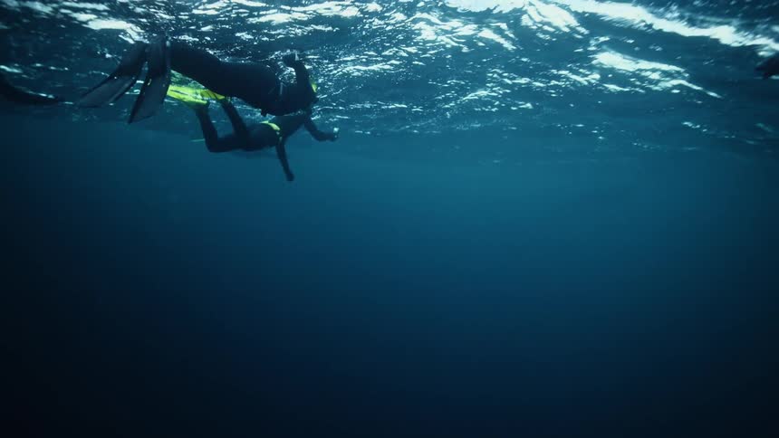 Underwater view of snorkelers floating on the calm, deep blue ocean surface in slow motion