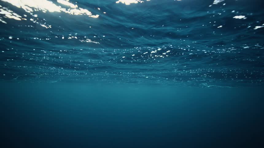An underwater view looking up at the serene surface of the deep blue ocean as sunlight filters through the gentle waves