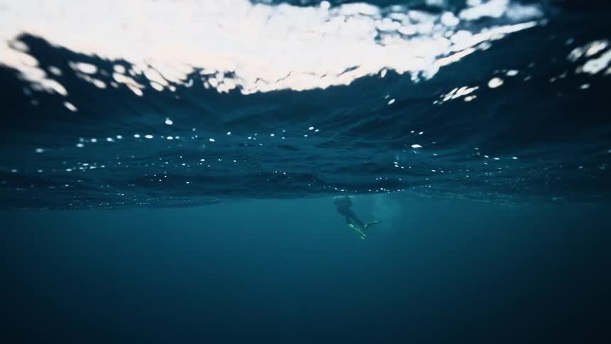 Mesmerizing underwater slow-motion shot of a scuba diver swimming beneath the ocean's surface