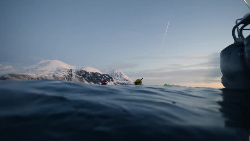 Slow-motion, water-level view of snorkelers in the frigid arctic ocean as the camera dips below the dark surface