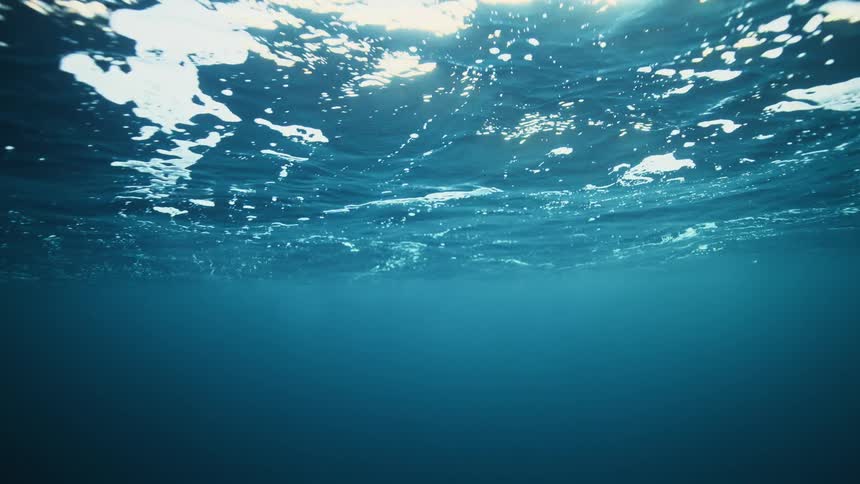 An underwater view looking up at the serene ocean surface as sunlight filters through the deep blue water