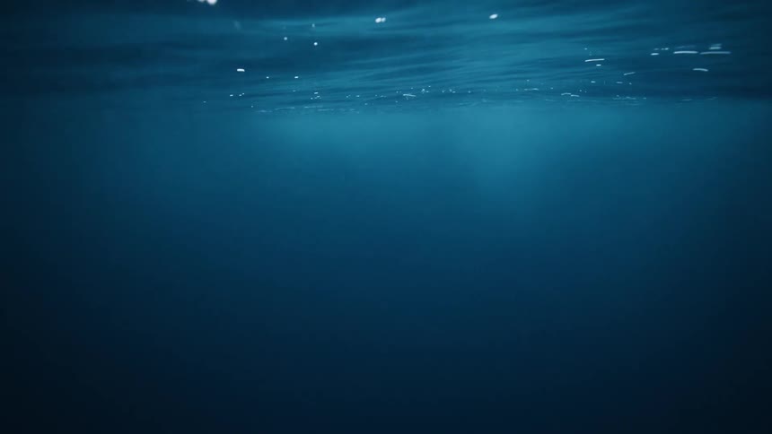 A serene underwater shot looks up towards the deep blue ocean's surface as light filters through