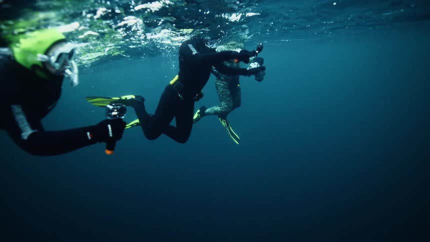 An underwater slow-motion shot of three divers floating at the surface of the deep blue ocean
