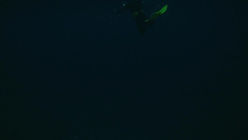 A snorkeler with bright fins swims on the surface of dark, mysterious waters as seen from below