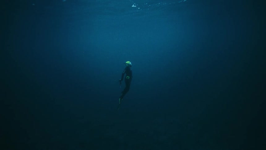 A scuba diver floats serenely in the vast deep blue ocean, slowly ascending towards the light of the surface
