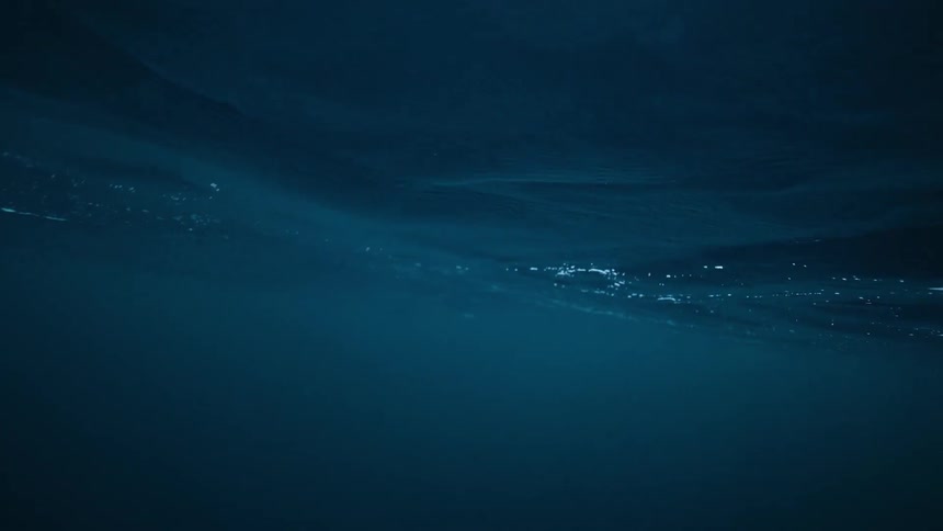 A serene underwater view shows a person in a wetsuit snorkeling below the calm surface of the deep blue sea