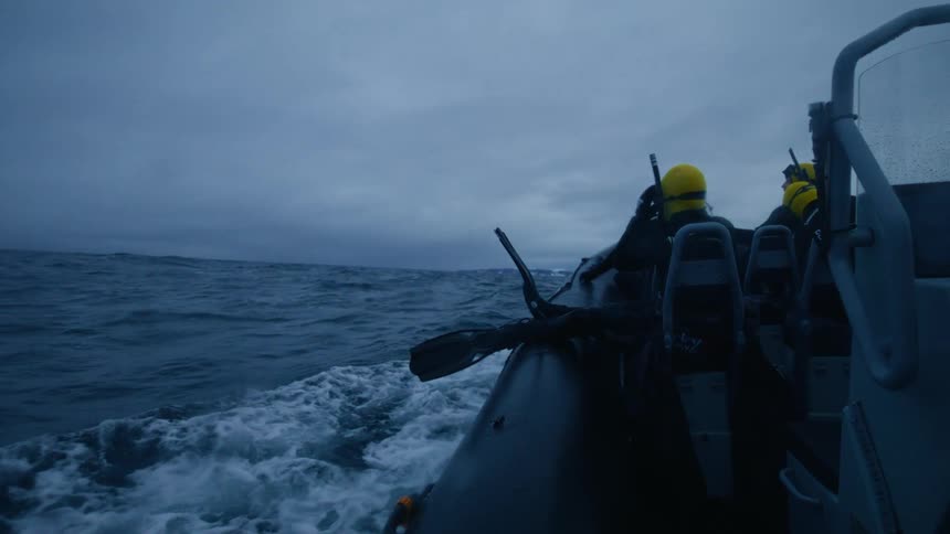 Slow motion shot of scuba divers on a rigid inflatable boat heading out into the cold, choppy ocean under an overcast sky