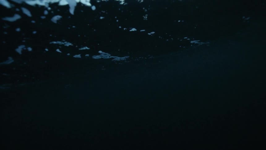 A mysterious underwater perspective captures the dark, rippling surface of the ocean in slow motion