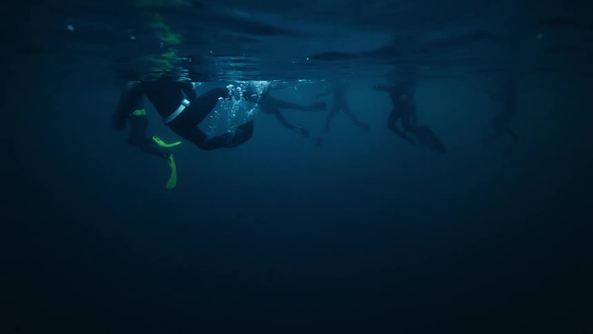 A group of scuba divers float on the surface of the deep blue ocean in a serene underwater slow-motion shot