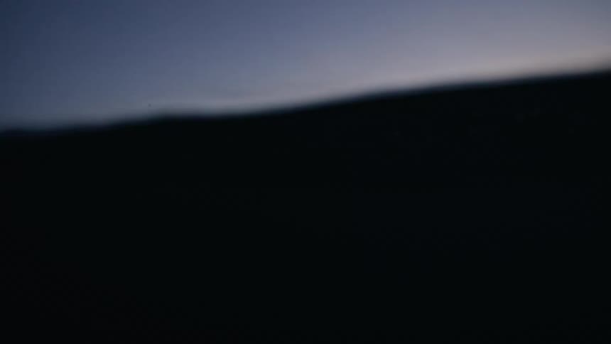 An immersive slow-motion view from within the ocean captures snow-capped mountains against a stunning sunset