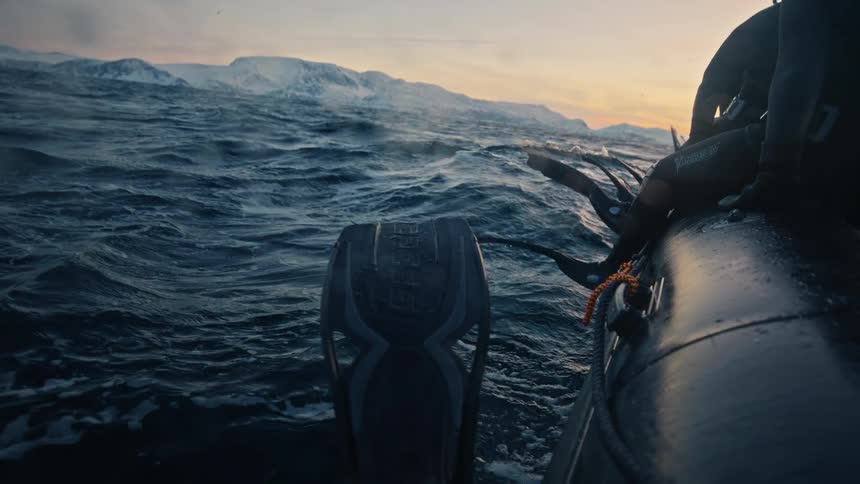 A thrilling first-person view from a boat shows divers encountering a majestic orca in the cold, choppy waters of the arctic at sunset