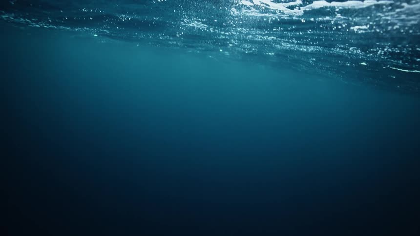 A serene underwater perspective captures the slow-motion dance of sunlight on the deep blue ocean's surface