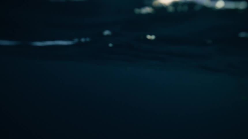 An immersive over-under shot captures the choppy surface of a cold sea and the dark abyss below, with majestic snow-covered mountains in the distance